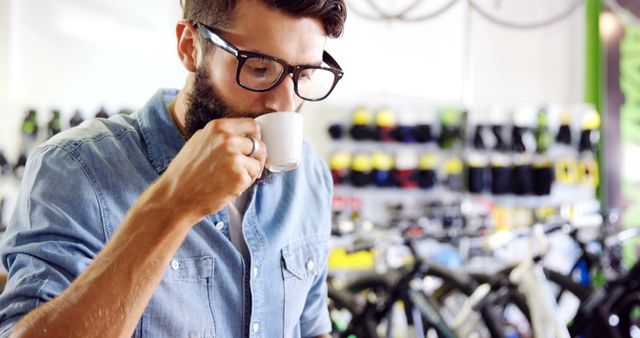 Man Wearing Glasses Drinking Coffee in Bicycle Shop - Download Free Stock Images Pikwizard.com