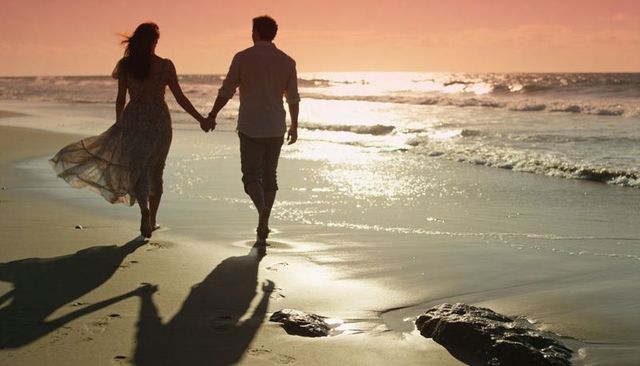 Walking couple holding hands at sunset beach silhouette, romantic dusk shoreline stroll