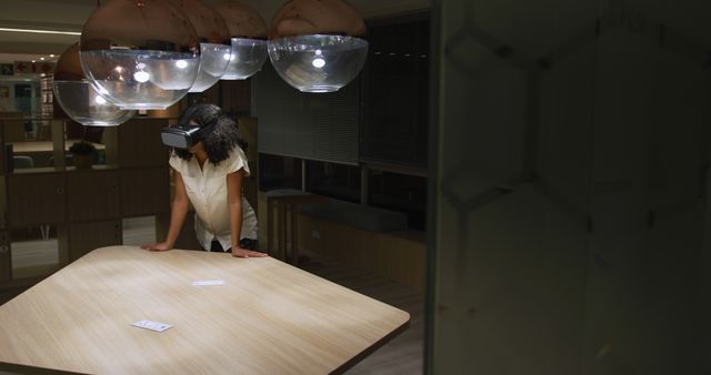 A woman using a virtual reality headset leaning on a wooden table in a modern office environment. Suitable for use in articles or projects related to innovative technology, virtual reality, modern workplace setups, and futuristic office spaces.
