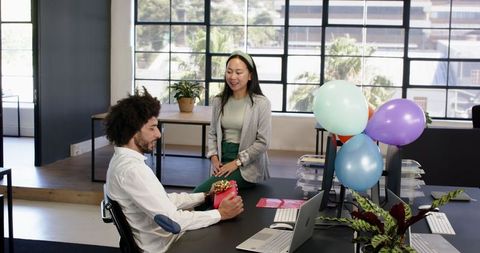 Office celebration: diverse coworkers sharing gift in decorated workspace