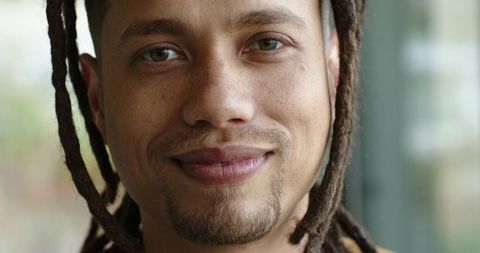 Close-up portrait smiling mid-adult man with dreadlocks and goatee, natural window light, warm bokeh
