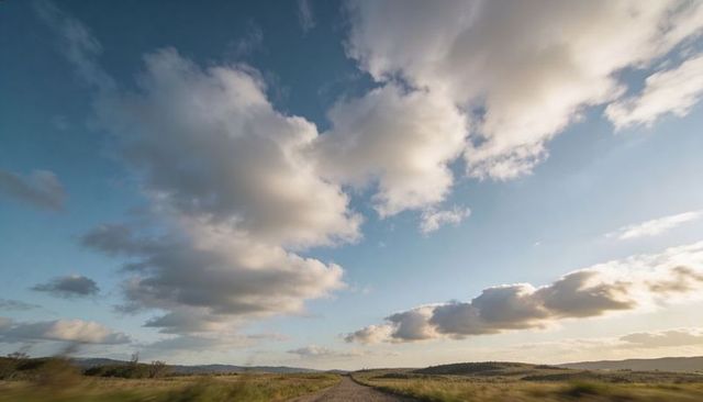 Gravel road leading through sunlit open meadow under dramatic cumulus clouds at golden hour