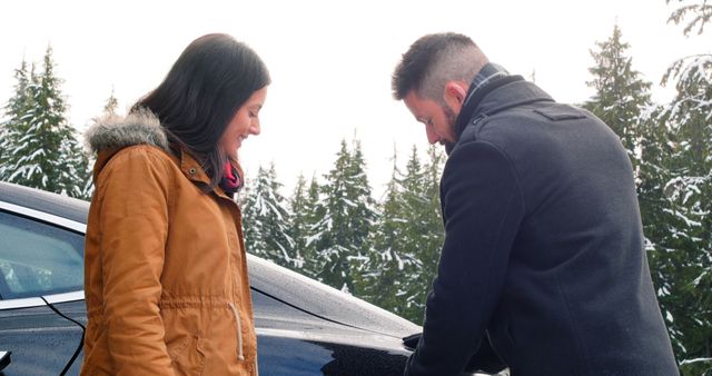 Smiling couple talking while charging the electric car on a snowy day