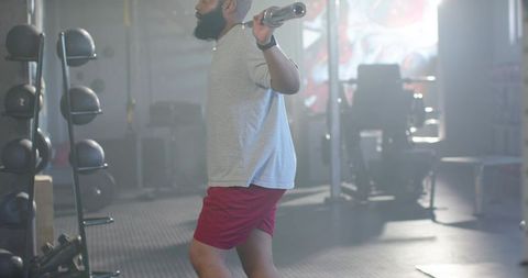 Man performing barbell lunge in gym wearing red shorts backlit strength training routine