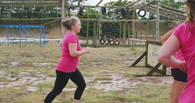 Determined plus size caucasian woman in pink t shirt running across bootcamp training course. Female fitness, friendship, challenge and healthy lifestyle.