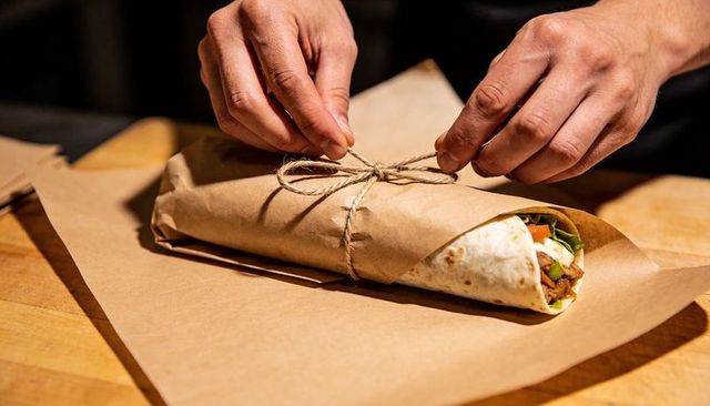 Chef tying twine on kraft-paper wrapped tortilla on wooden countertop for rustic takeaway
