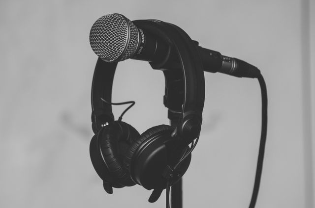 Detailed image perfect for music production or podcast promotional materials, highlighting professional audio equipment such as a microphone and headphones draped over a stand in a monochromatic style. Great for illustrating themes related to sound recording, broadcasting, or audio technology.