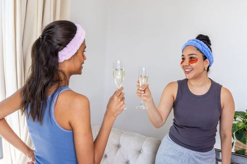 Diverse friends clinking champagne flutes during at-home spa night with eye patches