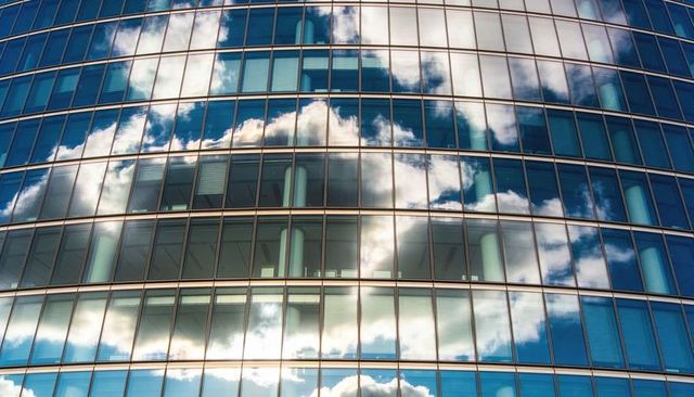 Curved glass facade reflecting clouds and revealing office interior with columns