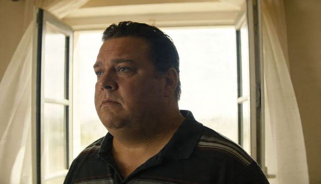Midlife man standing by open window, gazing contemplatively in warm diffused daylight