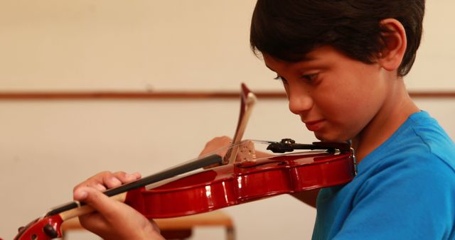 Young boy deeply focused on playing violin in a classroom setup showing dedication to learning music. Can be used for educational content, music lessons, youth talent, and practice-themed materials.