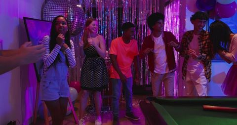 Teen friends dancing under disco ball at neon party with metallic fringe backdrop