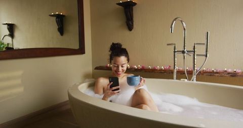Happy Woman Relaxing in Bathtub with Coffee and Smartphone
