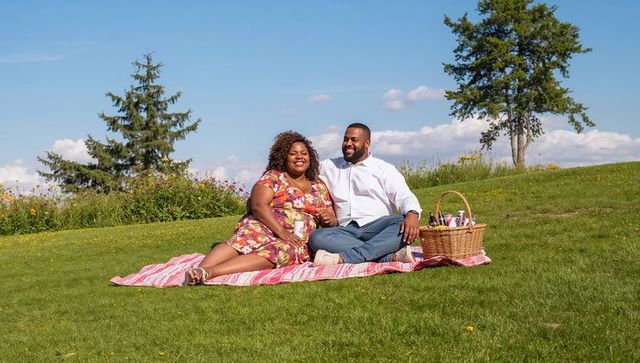 Couple enjoying sunny picnic on meadow blanket with wicker basket and wildflowers