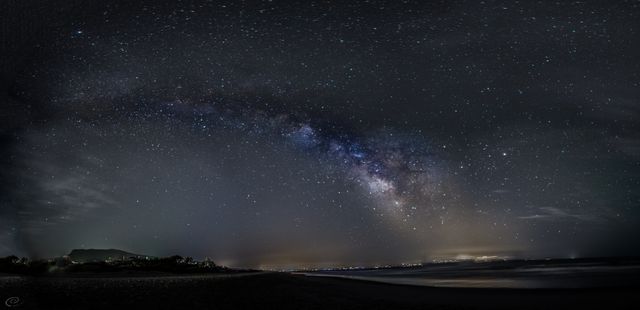 Milky Way spanning across dark sky over tranquil beach. Perfect for prints, nature-themed decor, teaching materials on astronomy, or inspirational content about nature and the universe.