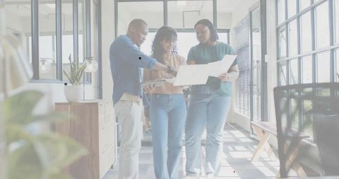 Three colleagues reviewing blueprint and digital plans in bright modern glass office