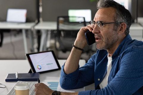 Mature professional reviewing data on tablet while taking phone call in modern office