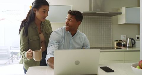 Remote couple working together at sunlit kitchen island with laptop and coffee