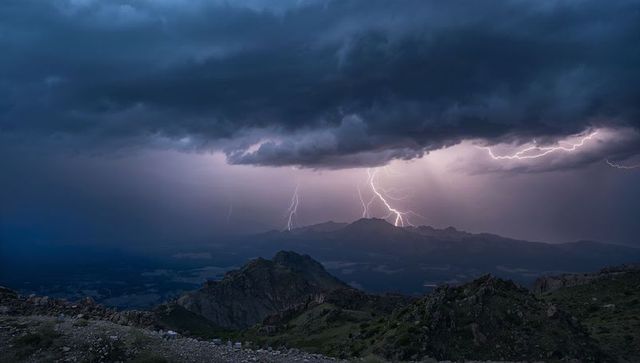Lightning striking mountain ridge at dusk with dramatic storm clouds and alpine peaks