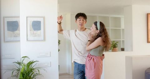 Couple leaning and laughing in sunlit modern home with greenery and wall art