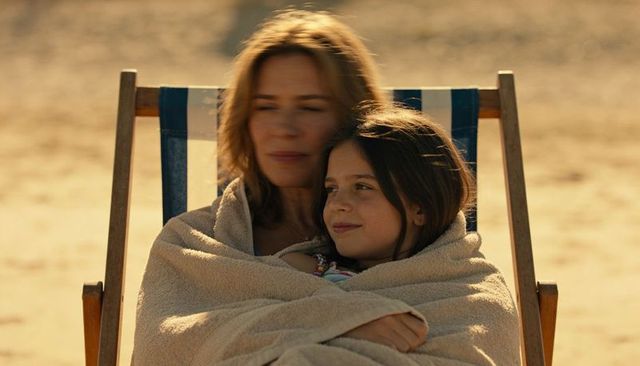 Mother wrapping daughter in towel on striped deck chair at beach during golden hour