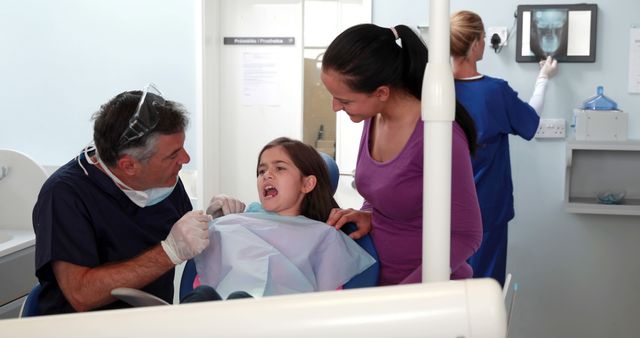 Girl at dental clinic sitting in chair with dentist and her mother - Download Free Stock Images Pikwizard.com