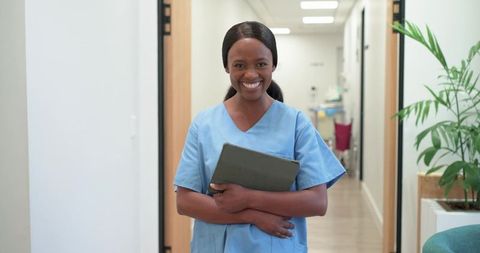 Smiling african nurse holding tablet while standing in modern clinic corridor
