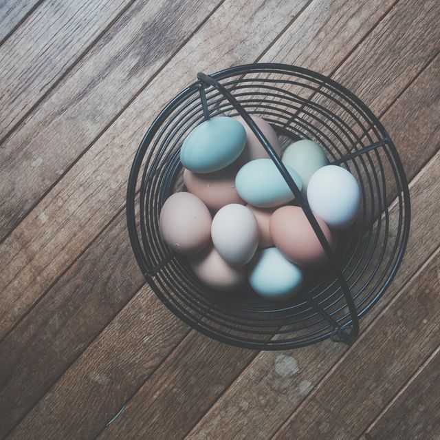 Assorted farm fresh eggs placed in a wire basket, set on a vintage wooden floor. Perfect for use in organic food promotions, farm-to-table concepts, and rustic kitchen decor ideas. Highlights the variety and natural beauty of farm fresh produce.