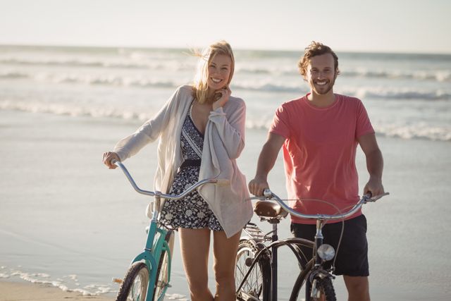 Portrait of smiling couple with bicycles standing at beach during sunny day