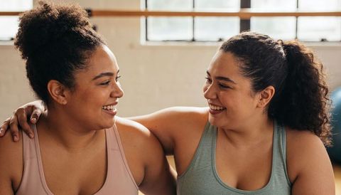 Smiling workout partners hugging on bench in fitness studio promoting support and wellness