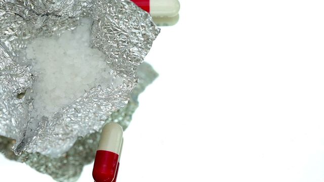 Image shows cocaine in foil along with capsules on a reflective white surface. Perfect for illustrating concepts related to substance abuse, addiction issues, or drug safety education. Can be used in articles, educational brochures, or awareness campaigns focusing on drug misuse.