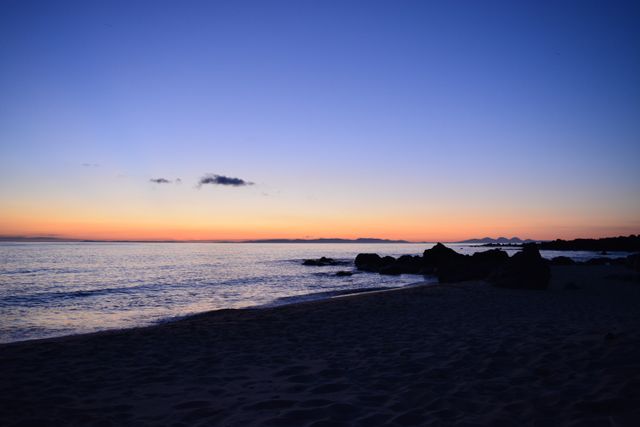 Serene Sunset Over Calm Ocean With Sandy Beach And Silhouetted Rocks - Download Free Stock Photos Pikwizard.com