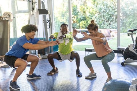 Multiracial friends doing group squats in bright gym for training, teamwork and wellness