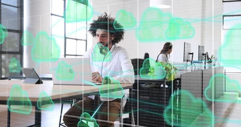 Working man in modern office typing on laptop wearing headset with cloud computing overlay