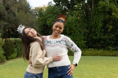 Smiling diverse friends hugging on garden lawn wearing festive headbands and knit sweaters