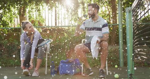 Male and Female Tennis Players Resting Courtside on Sunny Day
