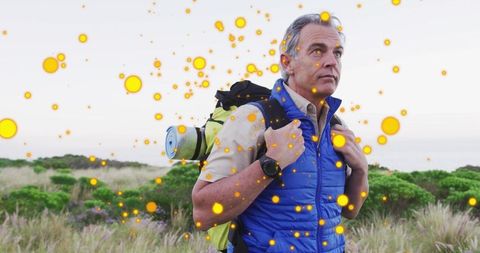Mature hiker surveying coastal dunes carrying backpack with golden glow overlay