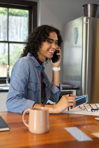 Non-binary person smiling while talking on phone and arranging paint swatches at counter