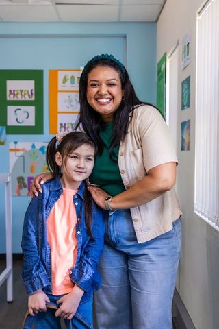 Smiling diverse female teacher embracing young student in colorful elementary classroom