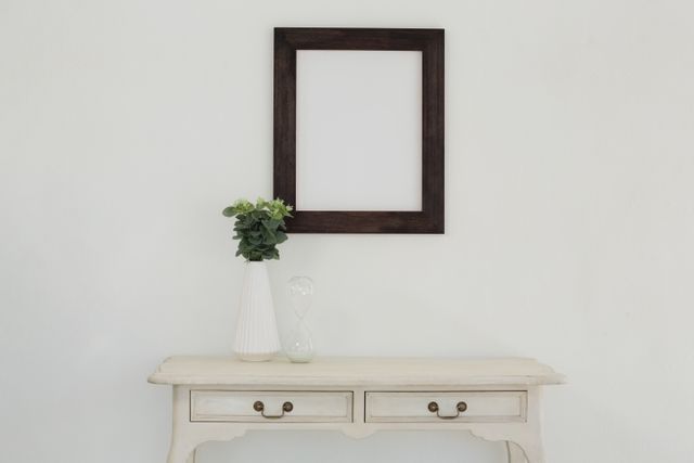 Perfect for illustrating minimalist interior design concepts, this image showcases a wooden frame and a vase with greenery against a white wall. Ideal for home decor blogs, design magazines, and promotional materials for furniture stores.