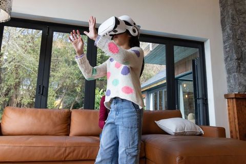 Asian child wearing VR headset playing in modern family living room with leather sofa