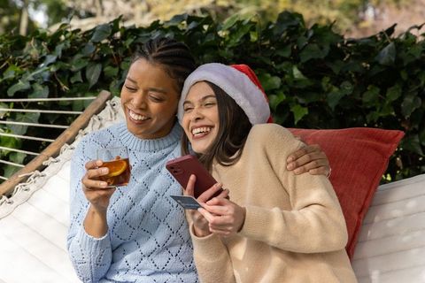 Multiracial friends laughing on hammock doing holiday online shopping with credit card