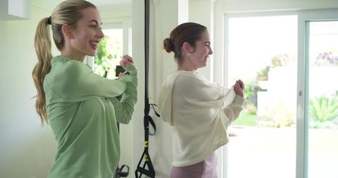 Two women stretching with trx suspension straps in bright home studio