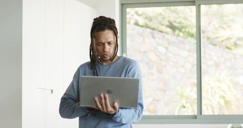 Focused man working on laptop in bright minimalist home office with large window