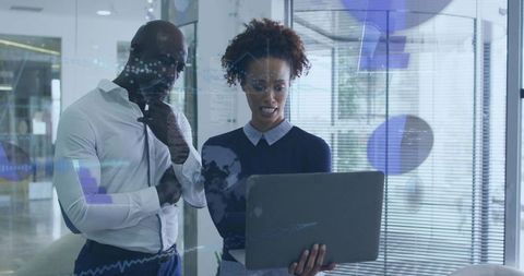 Professionals reviewing data on laptop in modern glass office collaborating on analytics