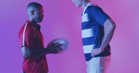 Athletes holding rugby ball facing each other in neon magenta studio lighting high-contrast