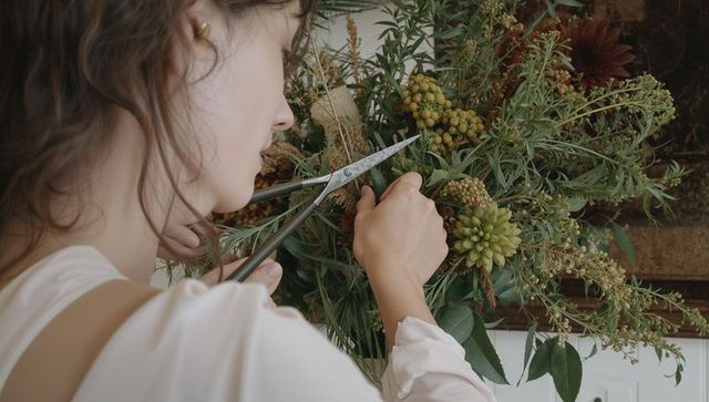 Florist trimming lush greenery with floral shears in rustic home studio workshop