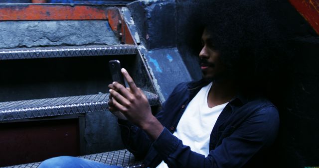 Young Man with Afro Hair Using Smartphone on Urban Stairs - Download Free Stock Images Pikwizard.com