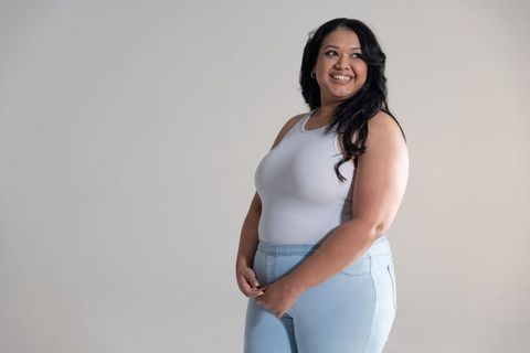 Confident woman in her 30s smiling and glancing right standing in white tank and jeans