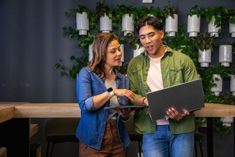Two diverse coworkers discussing project at modern coworking space with vertical garden wall